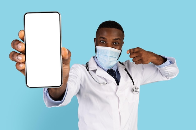 Check this app black doctor wearing medical mask pointing at blank smartphone