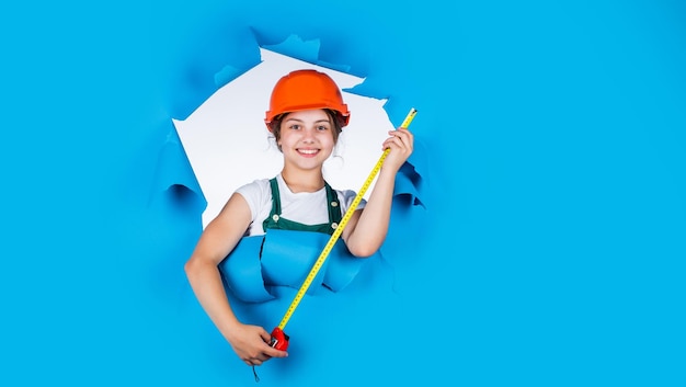 Checking every detail for defects kid wear helmet on construction site teen girl builder with building tool tape measure child on repairing work concept of renovation in workshop