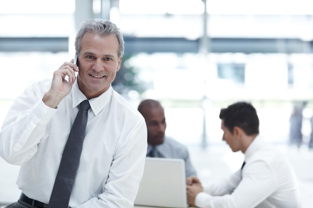 Checking in on the family Portrait of a mature businessman talking on his cellphone in front of two younger colleagues