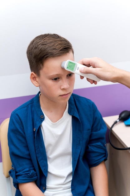 Checking temperature with infrared forehead thermometer. Boy at pediatrician`s consultation.