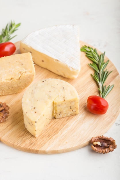 Cheddar and various types of cheese with rosemary and tomatoes on wooden board on a white background Side view selective focus