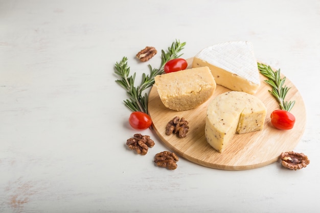 Cheddar and various types of cheese with rosemary and tomatoes on wooden board on a white background.