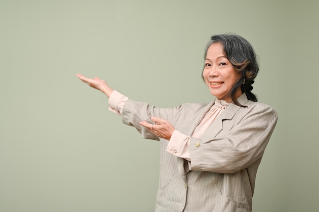 Cheerful 60s aged Asian woman opening empty hands aside on isolated green background