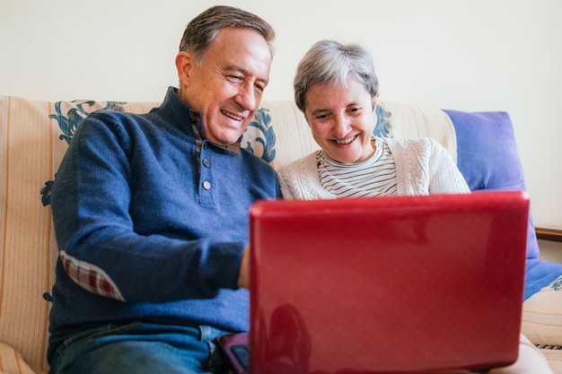 A cheerful adult couple sitting on a couch and watching a program on a laptop