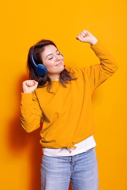 Cheerful adult enjoying song on headphones and dancing to have fun. Woman feeling happy and listening to music on headset while doing dance moves smiling. Positive active person