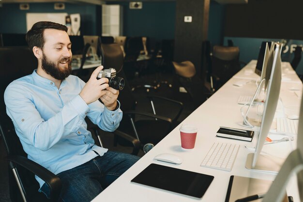 Photo cheerful adult man sitting and scrolling photo camera at desk in office