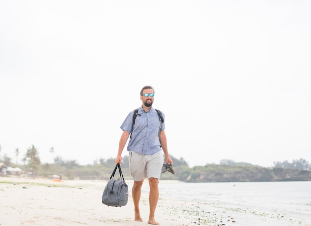 Cheerful adult man with bag having fun on the tropical beach