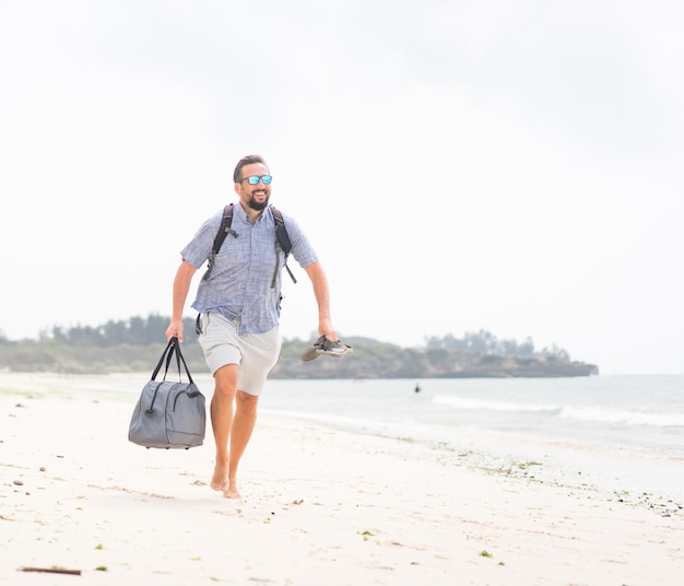 Cheerful adult man with bag having fun on the tropical beach