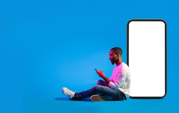 Cheerful african american man using smartphone on blue