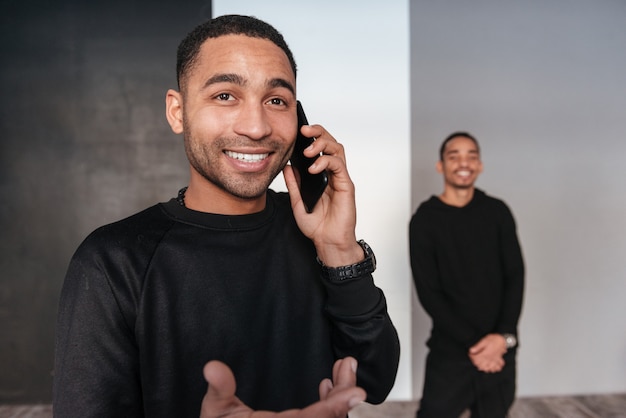 Cheerful african young man stading and talking on mobile phone