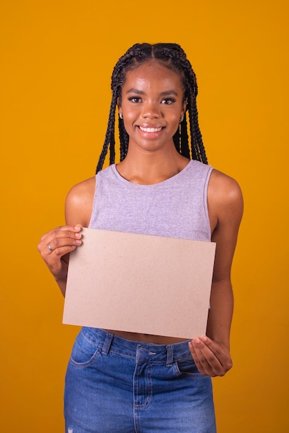 Cheerful afro american woman showing blank board over yellow background