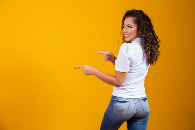 Cheerful afro woman points to copy space, discusses amazing promo, gives place or direction. Woman with her back pointing to the side