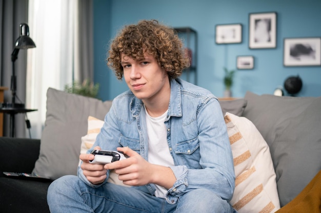 Cheerful american man resting in living room sitting on sofa playing video games using joysticks