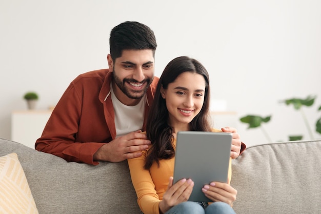 Cheerful arabic couple using digital tablet holding computer at home