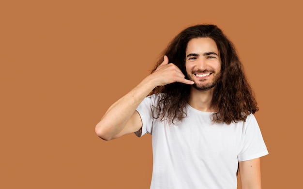 Cheerful arabic young man gesturing call me against beige backdrop