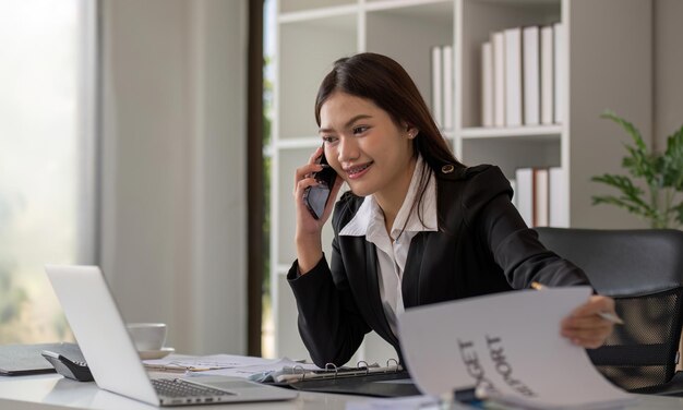 Cheerful asian businesswoman talking on the phone working in modern office happy asian businesswoman