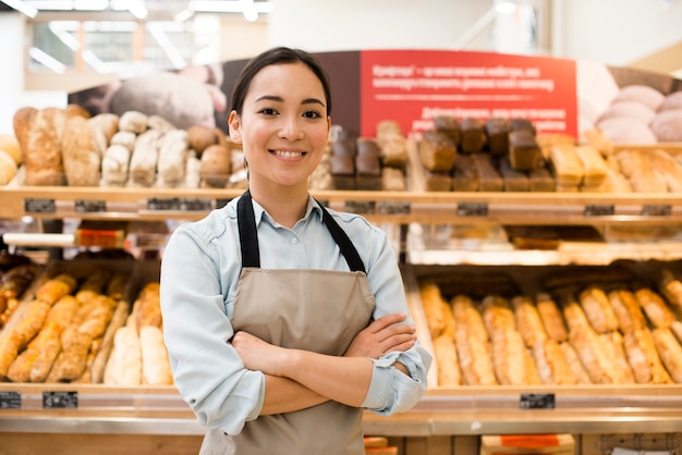 Cheerful Asian female bakery seller with arms crossed in supermarket