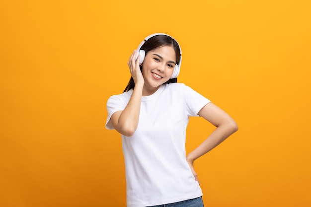 Cheerful asian female teenager listen to the music with white headphone dancing on isolated yellow background. Beautiful young woman in hand touch a wireless headphone having fun with music.