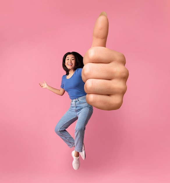 Cheerful Asian Girl Jumping In Air And Showing Thumb Up