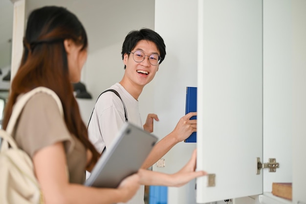 Cheerful Asian male college student talking with his friend at a school corridor