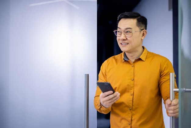 Cheerful asian male professional using his smartphone in a brightly lit modern office environment