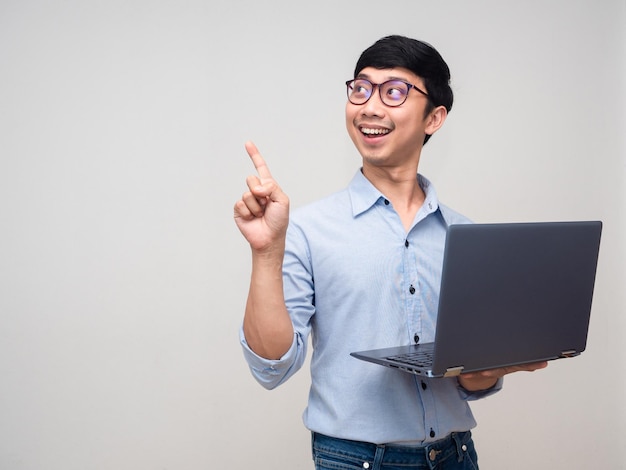 Cheerful asian man glasses hold laptop and gesture point finger isolated