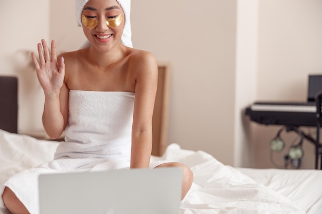 Cheerful asian woman using laptop after shower at home