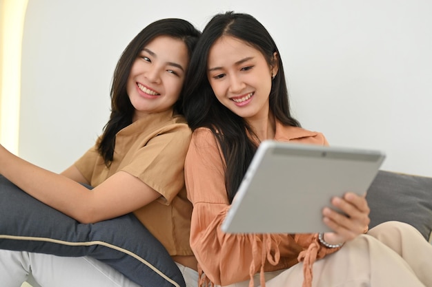 Cheerful asian women sits in living room and watching movie on digital tablet together