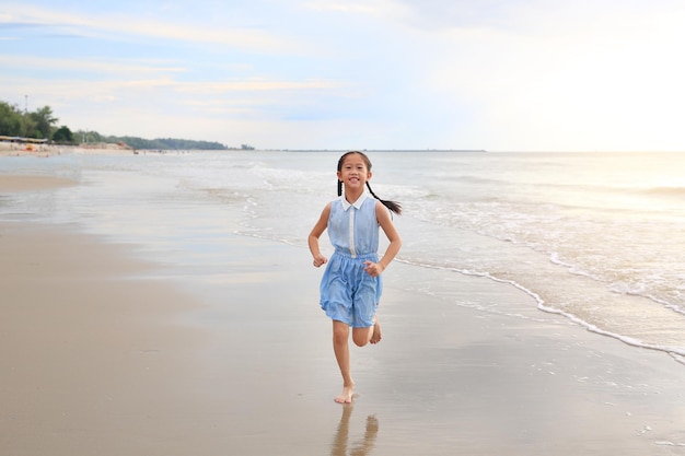 Cheerful Asian young girl child having fun running on tropical sand beach at sunrise