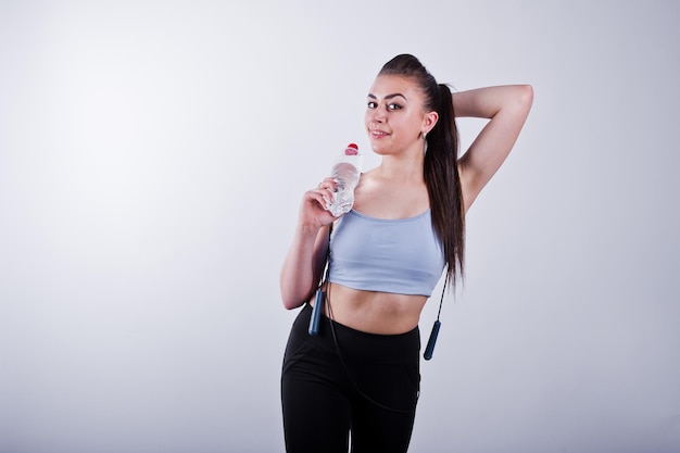 Cheerful attractive young fitness woman in top and black leggings with jump rope and bottle of water isolated over white background