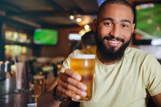 Cheerful attractive young man drinking beer in pub