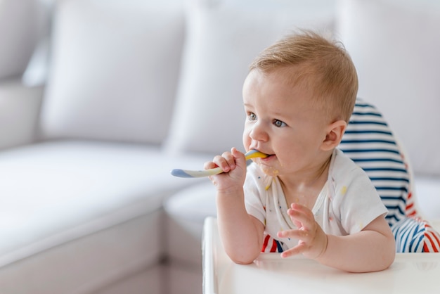 Cheerful baby child eats food itself with spoon.