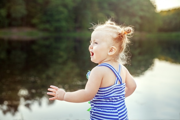 Cheerful baby girl playing near the lake. 