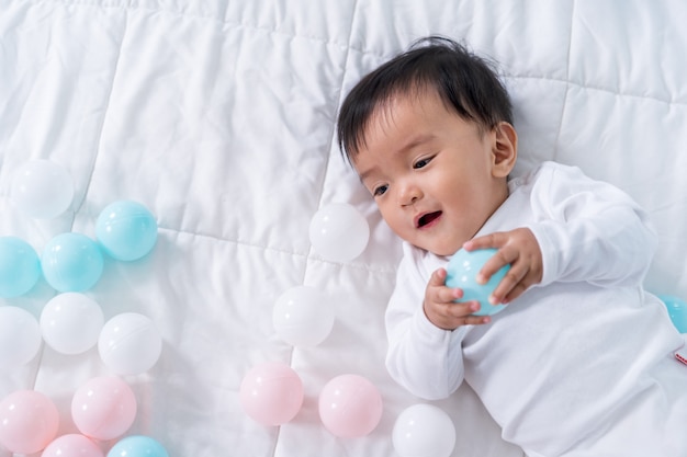 Cheerful baby playing color ball on bed