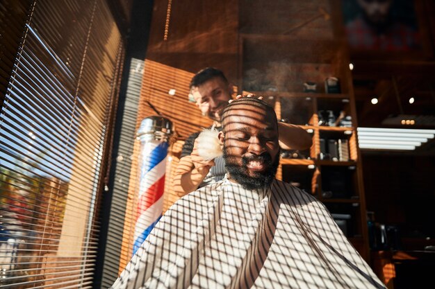 Cheerful barber applying talcum powder on client neck