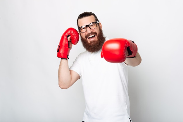 Cheerful bearded hipster man in casual punching with red boxing gloves