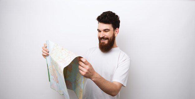 Photo cheerful bearded man using map standing over white background, travel concept