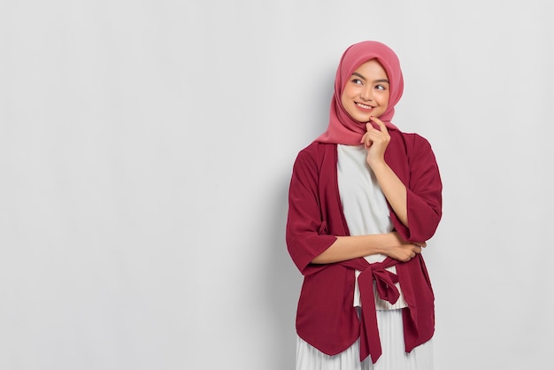 Cheerful beautiful Asian woman in casual shirt looking away at copy space creating new idea solution isolated over white background