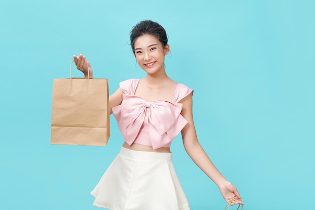 Cheerful beautiful Asian woman holding craft shopping bags on light cyan background