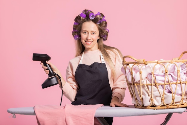 A cheerful beautiful blonde woman holds a clothes steamer performs household laundry duties