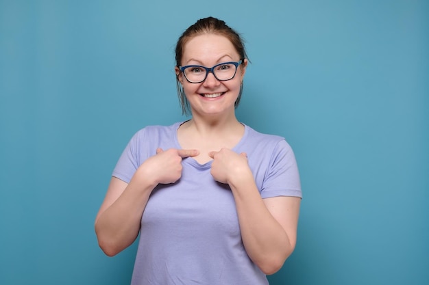 Cheerful beautiful blonde young woman on glasses looks joyful and points at herself