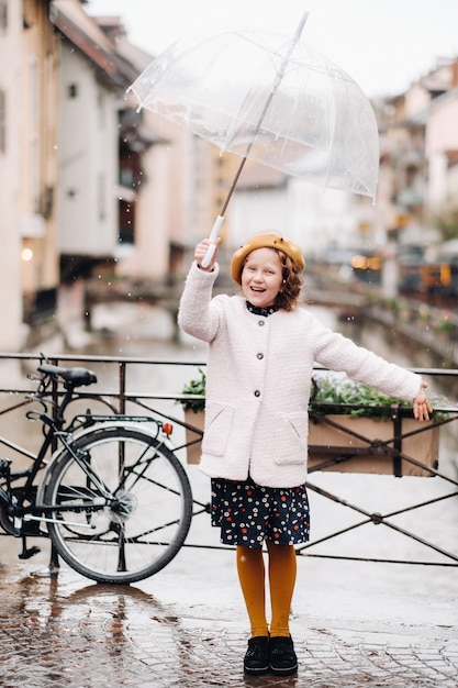 Cheerful beautiful girl in a coat with a transparent umbrella in Annecy