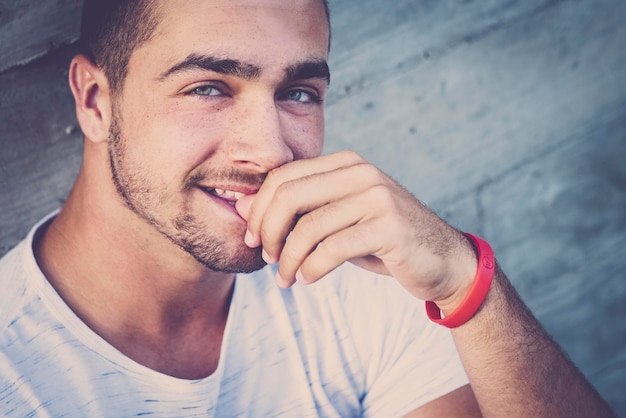 Cheerful beautiful young boy teenager caucasian people sitting with a urban city wall in background looking at the camera smiling in handsome style blue eyes