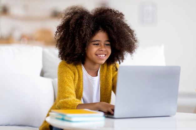 Cheerful black girl schooler doing homework using computer