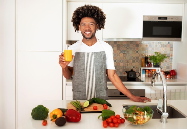 Cheerful Black Guy Holding Glass Of Orange Juice In Kitchen