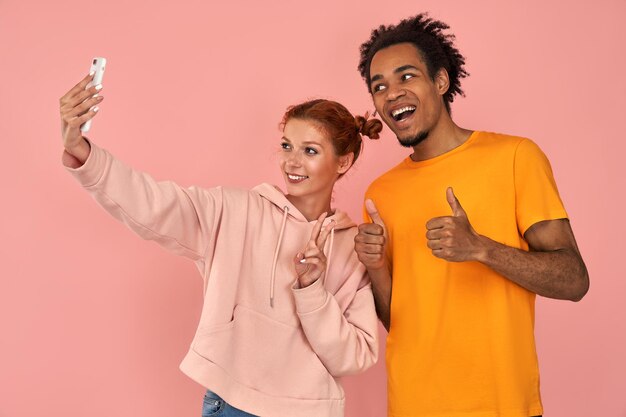 Photo cheerful black man laughs sincerely poses for selfie with ginger girlfriend makes peace sign gesture