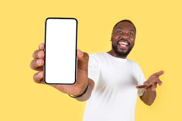 Cheerful Black Man Showing Huge Smartphone Empty Screen Yellow Background