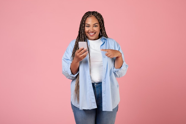 Cheerful Black Plump Lady Using Phone Standing Over Pink Background