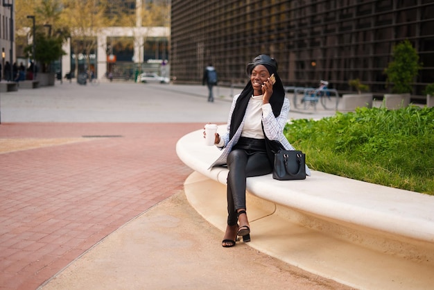 Cheerful black woman with takeaway coffee speaking on smartphone