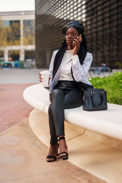 Cheerful black woman with takeaway coffee speaking on smartphone